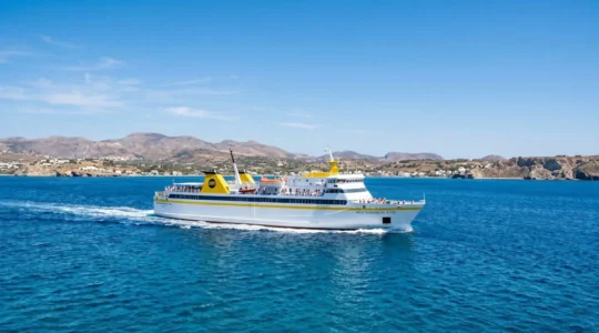 Ein modernes weiß-gelbes Fährschiff von Corsica Ferries fährt bei strahlendem Sonnenschein über das tiefblaue Mittelmeer mit Küstenlandschaft im Hintergrund